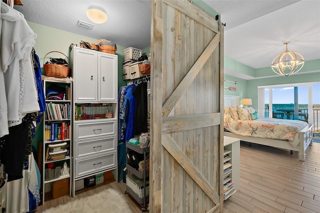 walk in closet with a barn door, a chandelier, and light hardwood / wood-style floors