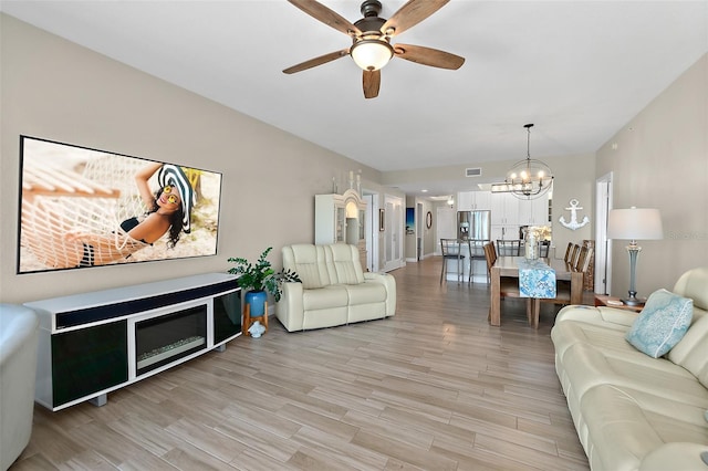 living room with ceiling fan with notable chandelier and light hardwood / wood-style floors