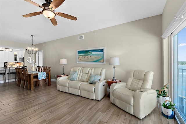 living room with ceiling fan with notable chandelier and light wood-type flooring