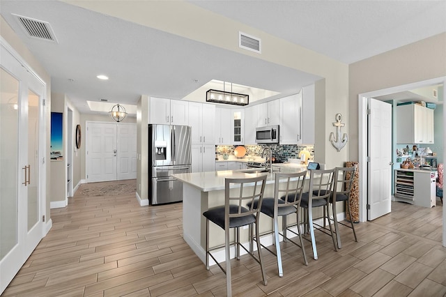 kitchen featuring sink, white cabinetry, kitchen peninsula, stainless steel appliances, and decorative backsplash