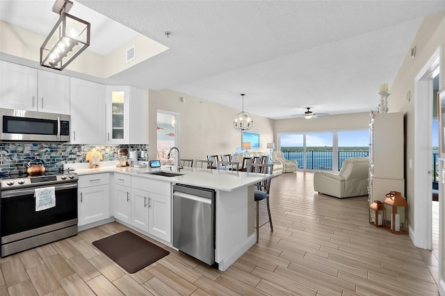 kitchen featuring appliances with stainless steel finishes, white cabinetry, sink, hanging light fixtures, and kitchen peninsula