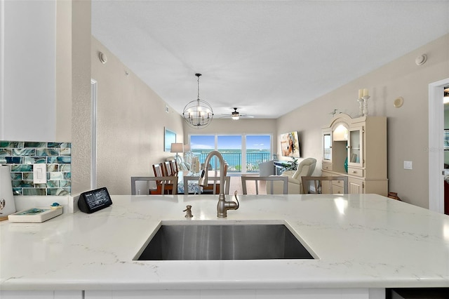 kitchen with pendant lighting, ceiling fan with notable chandelier, sink, and light stone counters