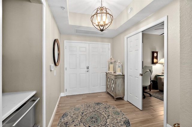 foyer entrance with a notable chandelier, light hardwood / wood-style floors, and a tray ceiling