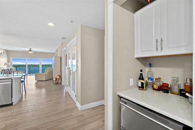 kitchen featuring white cabinetry, stainless steel dishwasher, ceiling fan, and light hardwood / wood-style flooring