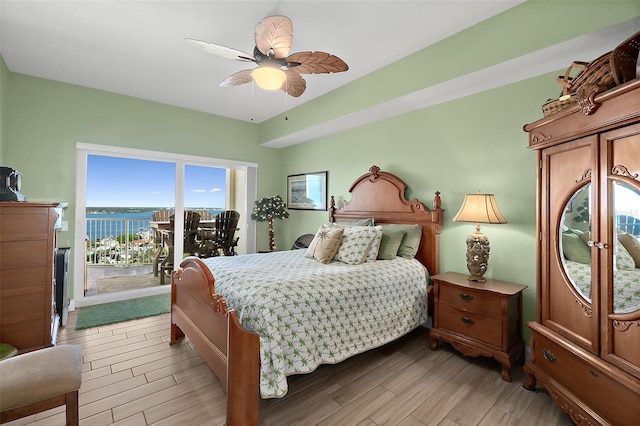 bedroom featuring access to exterior, light hardwood / wood-style flooring, ceiling fan, and a water view