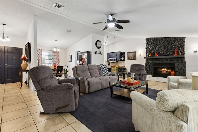 tiled living room with lofted ceiling, ceiling fan with notable chandelier, a stone fireplace, and a textured ceiling