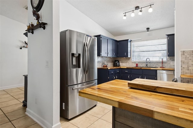 kitchen with stainless steel appliances, vaulted ceiling, sink, and butcher block countertops