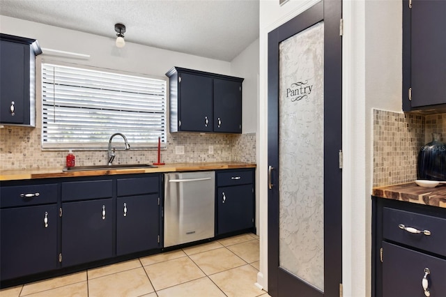 kitchen with sink, light tile patterned floors, wooden counters, dishwasher, and blue cabinets