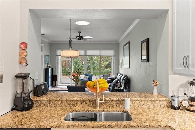 kitchen featuring light stone counters, sink, crown molding, and ceiling fan