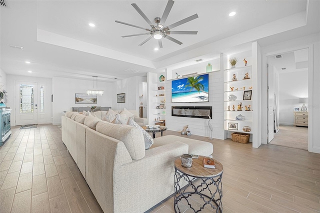 living room with ceiling fan, a tray ceiling, light hardwood / wood-style floors, and built in features