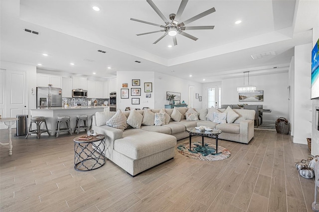 living room featuring ceiling fan, a tray ceiling, and light wood-type flooring