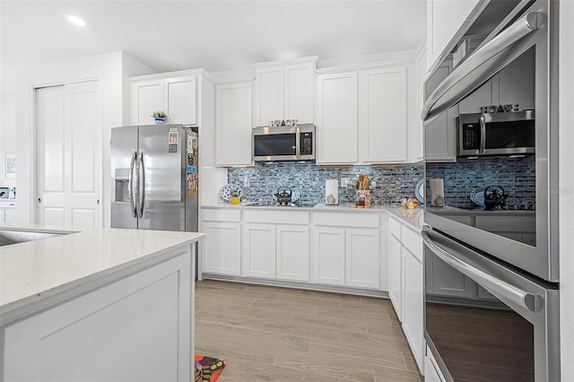 kitchen with tasteful backsplash, white cabinets, stainless steel appliances, light stone countertops, and light hardwood / wood-style flooring