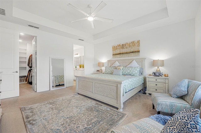 carpeted bedroom with a walk in closet, a raised ceiling, a closet, and ensuite bath