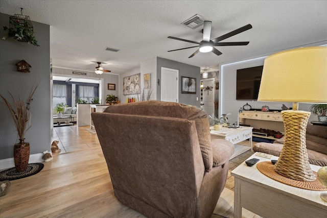 living room featuring ceiling fan, light hardwood / wood-style floors, and a textured ceiling