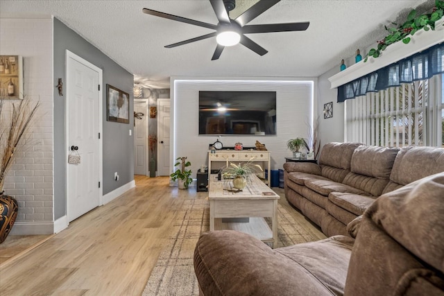 living room featuring ceiling fan, brick wall, a textured ceiling, and light wood-type flooring