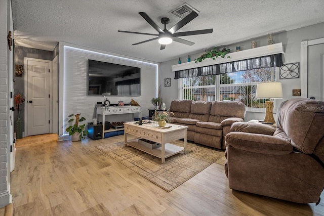 living room with ceiling fan, a textured ceiling, and light wood-type flooring