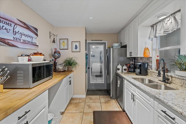 kitchen with sink, light tile patterned floors, appliances with stainless steel finishes, backsplash, and white cabinets