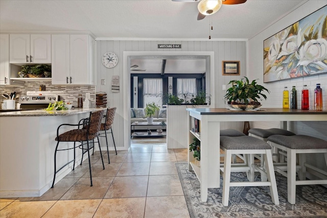 kitchen with light tile patterned floors, a breakfast bar, white cabinetry, stainless steel range with electric stovetop, and tasteful backsplash