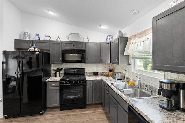 kitchen featuring sink, light hardwood / wood-style flooring, black appliances, decorative backsplash, and vaulted ceiling