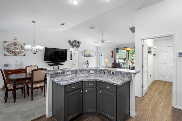 kitchen with light stone counters, vaulted ceiling, hanging light fixtures, hardwood / wood-style floors, and ceiling fan with notable chandelier