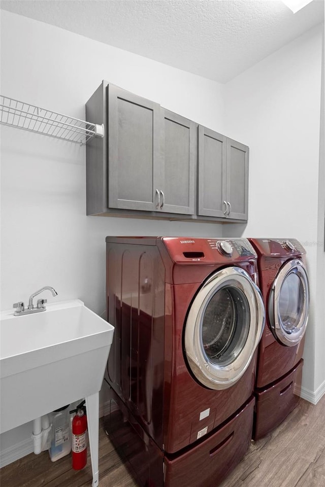 clothes washing area featuring cabinets, washing machine and dryer, a textured ceiling, and light wood-type flooring