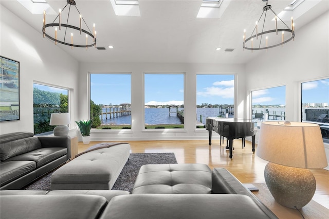 living room featuring a water view, a skylight, a chandelier, a wealth of natural light, and light hardwood / wood-style floors