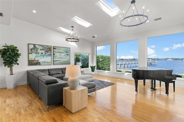 living room featuring a notable chandelier, light hardwood / wood-style flooring, vaulted ceiling with skylight, and a water view