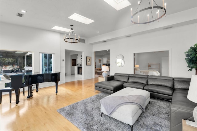 living room with a towering ceiling, wood-type flooring, a skylight, and a notable chandelier