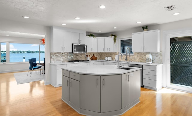 kitchen featuring white cabinets, light hardwood / wood-style floors, stainless steel appliances, a water view, and a center island with sink