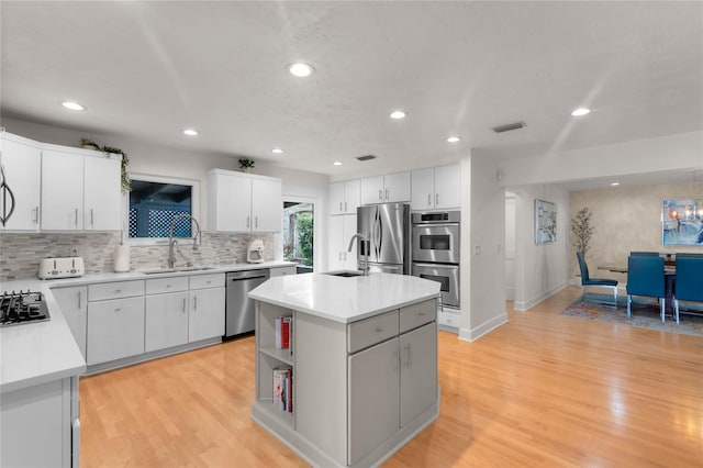 kitchen with appliances with stainless steel finishes, white cabinetry, sink, a center island, and light wood-type flooring