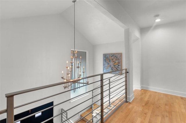 hall with an inviting chandelier, wood-type flooring, and lofted ceiling