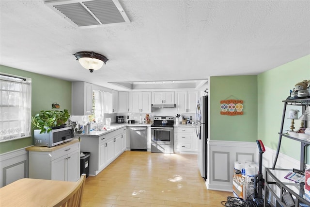 kitchen with appliances with stainless steel finishes, a textured ceiling, light hardwood / wood-style flooring, and white cabinets