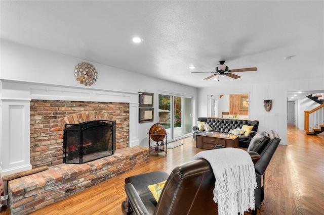 living room featuring a brick fireplace, ceiling fan, a textured ceiling, and light wood-type flooring