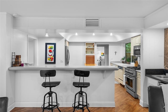 kitchen with sink, appliances with stainless steel finishes, a kitchen breakfast bar, light hardwood / wood-style floors, and kitchen peninsula