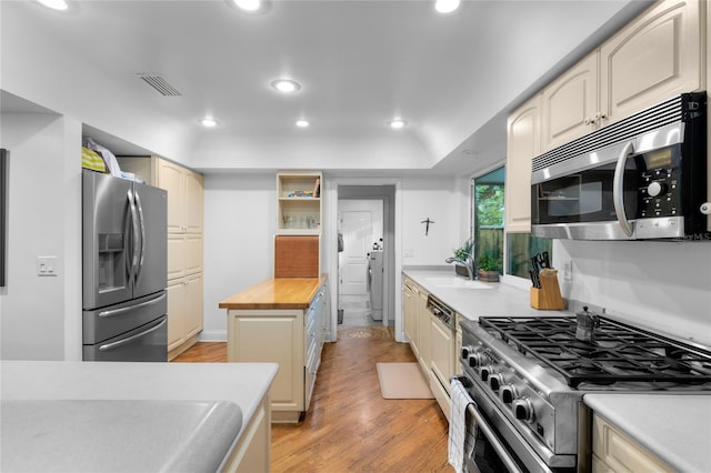 kitchen featuring wood counters, sink, light hardwood / wood-style flooring, stainless steel appliances, and cream cabinetry