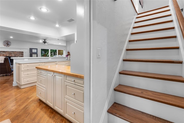 stairway featuring wood-type flooring, a stone fireplace, and ceiling fan