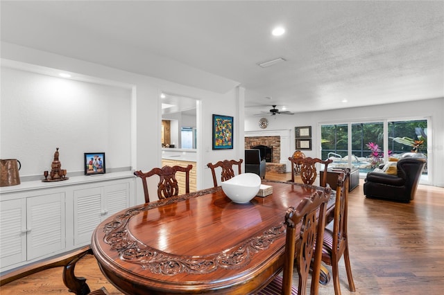 dining room featuring hardwood / wood-style flooring, ceiling fan, a fireplace, and a textured ceiling