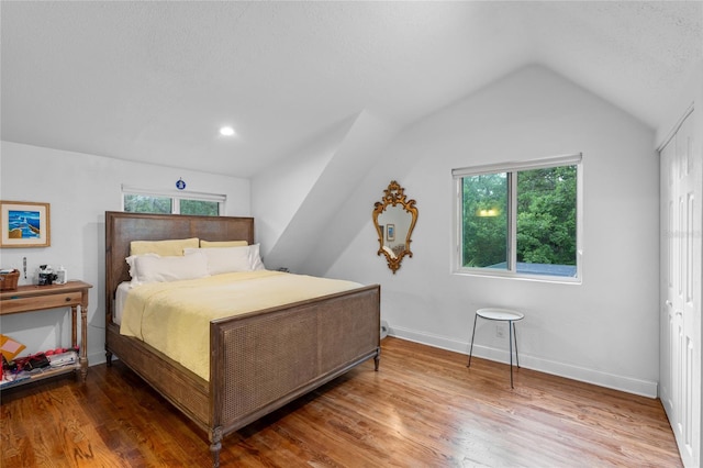 bedroom with a textured ceiling, vaulted ceiling, and wood-type flooring