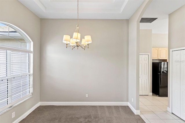 carpeted empty room with an inviting chandelier and a raised ceiling