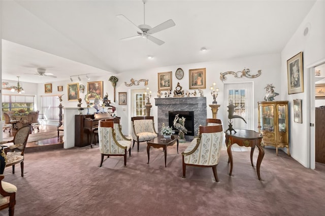 sitting room with lofted ceiling, rail lighting, a premium fireplace, dark colored carpet, and ceiling fan with notable chandelier