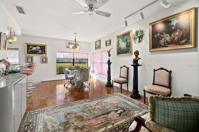 sitting room featuring rail lighting, ceiling fan with notable chandelier, and parquet floors