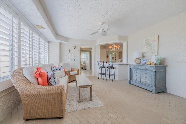 living room with ceiling fan with notable chandelier and a textured ceiling