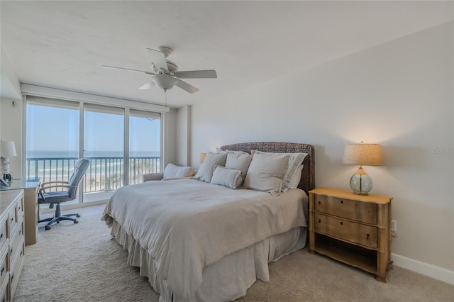 bedroom with a water view, light carpet, access to outside, ceiling fan, and a wall of windows