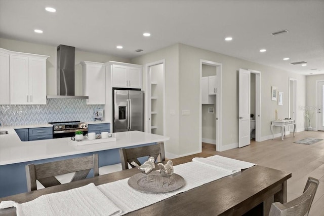 kitchen featuring white cabinetry, decorative backsplash, stainless steel appliances, wall chimney range hood, and light hardwood / wood-style flooring