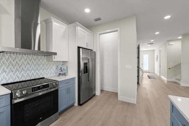 kitchen featuring light hardwood / wood-style flooring, appliances with stainless steel finishes, white cabinets, blue cabinets, and wall chimney exhaust hood