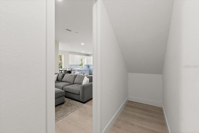 hallway featuring vaulted ceiling and light hardwood / wood-style flooring