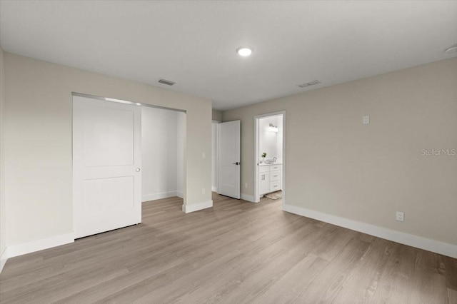 unfurnished bedroom featuring ensuite bathroom, light hardwood / wood-style floors, and a closet