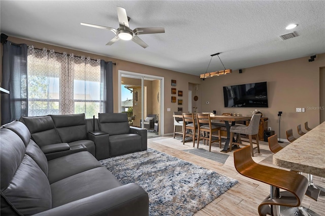 living room with ceiling fan, light hardwood / wood-style flooring, and a textured ceiling