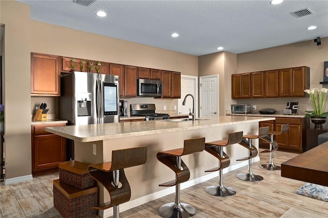 kitchen with a breakfast bar, sink, a center island with sink, a textured ceiling, and stainless steel appliances