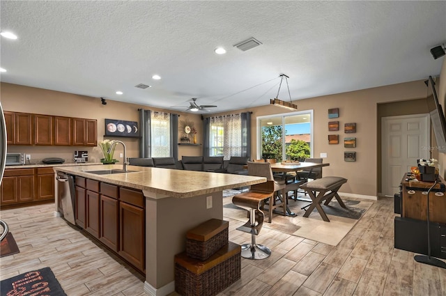 kitchen with pendant lighting, dishwasher, sink, a center island with sink, and a textured ceiling